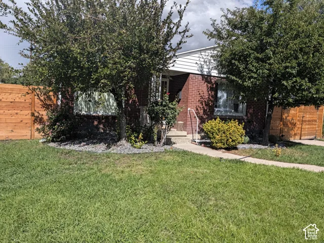 Brick exterior with white siding accents, mature trees, wood privacy fencing, and concrete walkway