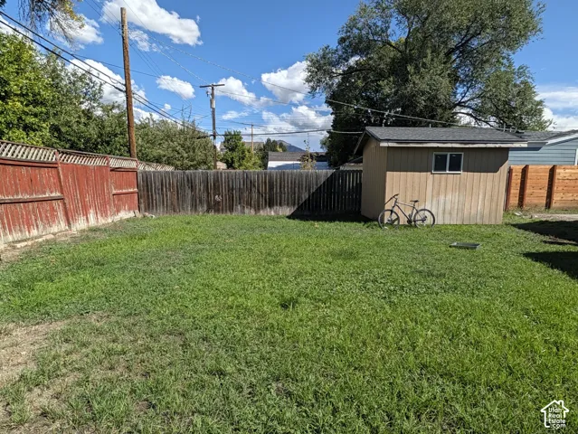 Fenced backyard with a storage shed featuring a single window and asphalt shingle roof