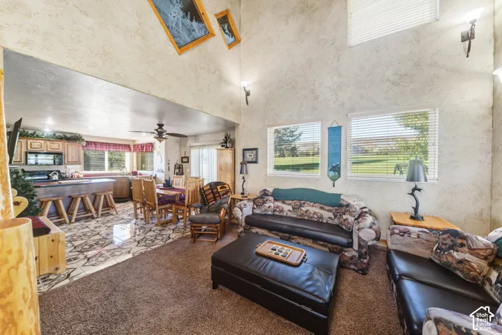 Vaulted ceiling with textured walls, dual windows, open concept design, kitchen with wood cabinetry, and a ceiling fan
