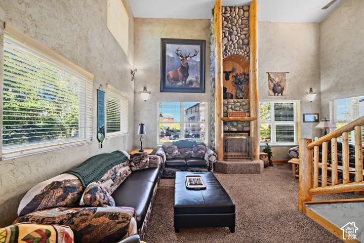 Vaulted ceiling, stone fireplace with log accents, multiple windows, textured wall finish, and a wood-finish staircase