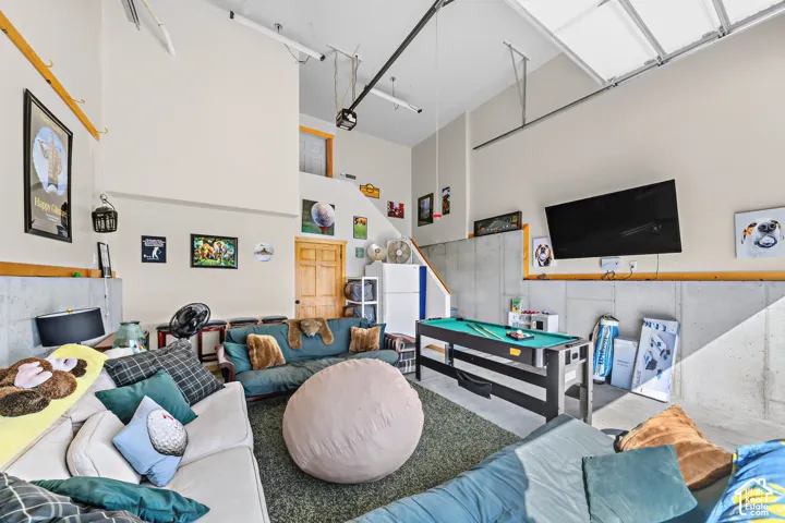 High ceilings with exposed structural elements, concrete wall paneling, and a wood-finish door