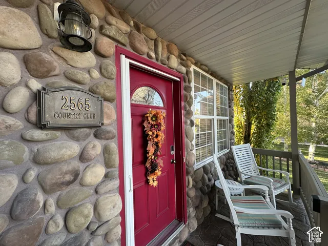 Stone veneer exterior with a covered porch featuring a red entry door, a multi-pane window, and an exterior wall lantern