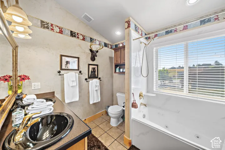 Dual sink vanity with gold-finish fixtures, a built-in jetted tub, tiled flooring, and a window with horizontal blinds