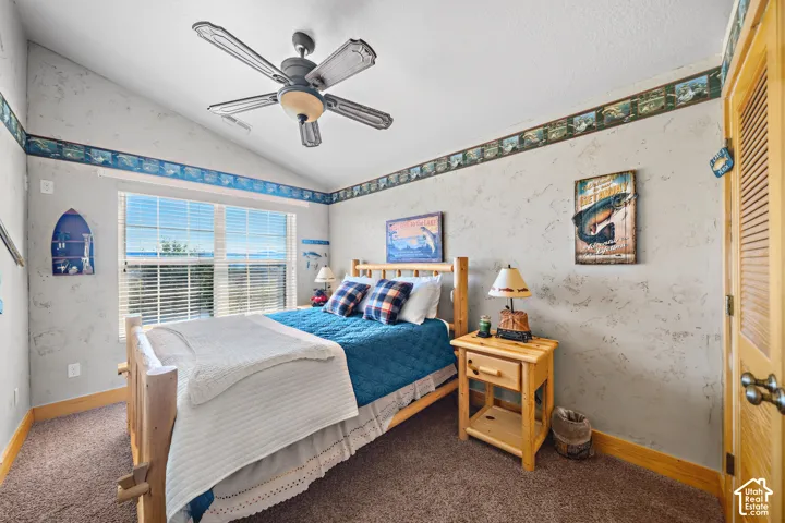 Vaulted ceiling, ceiling fan with light fixture, textured walls, wood-finish door, and large window with horizontal blinds