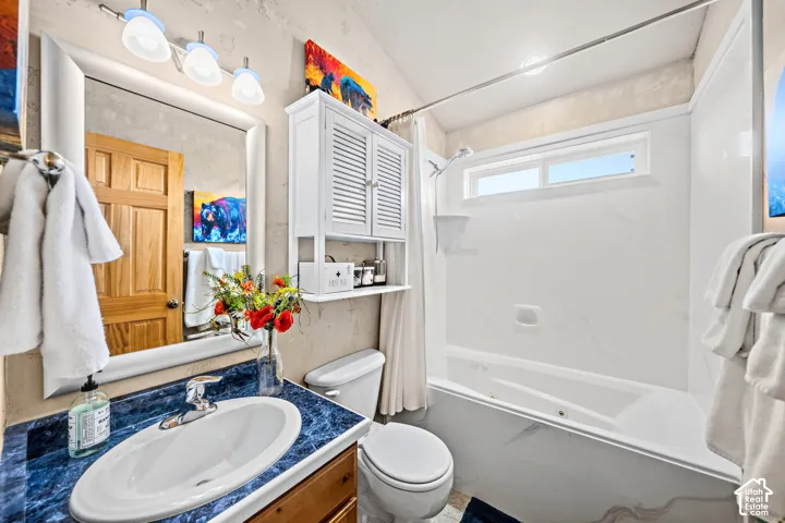 Vanity with a blue patterned countertop and oval sink, wall-mounted mirror, three-light fixture, built-in white storage cabinet, and a shower-over-tub combination with a transom window
