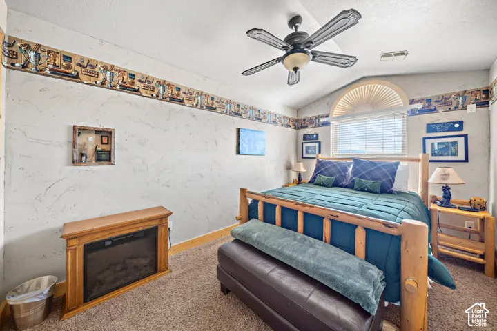Vaulted ceiling with a ceiling fan, wall-mounted electric fireplace, and a window with arched transom