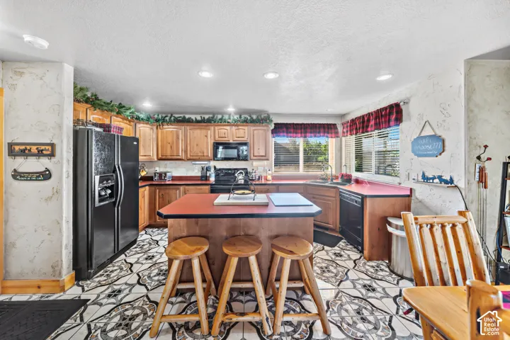 Kitchen featuring wood cabinetry, an island with seating, a built-in dishwasher, and recessed lighting