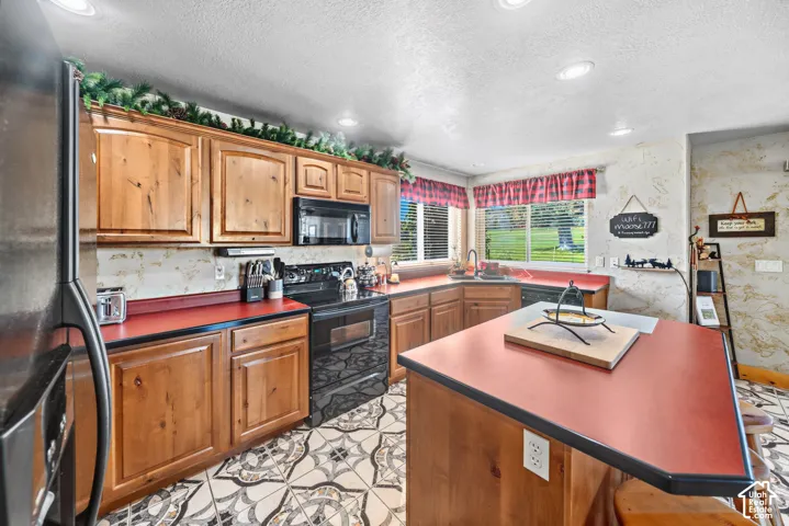 Kitchen featuring wood cabinetry, a center island with countertop, stainless steel refrigerator, black range, and patterned floor tile