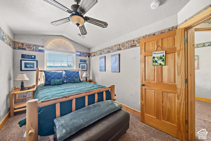 Vaulted ceiling with a ceiling fan, arched window with blinds, natural wood paneled door, and carpeted flooring