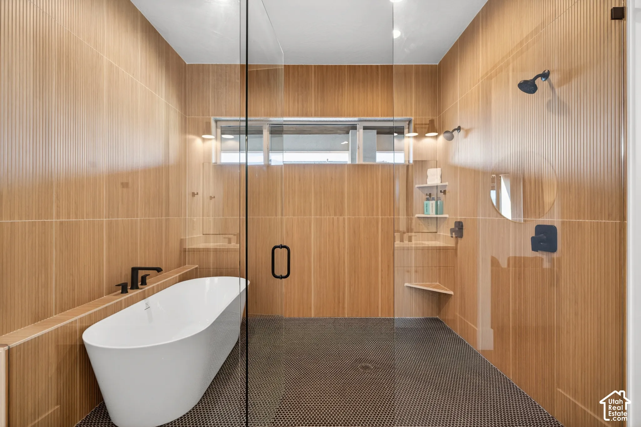 Freestanding soaking tub with matte black fixtures, glass-enclosed shower, wood-look tiled walls, and mosaic tiled floor