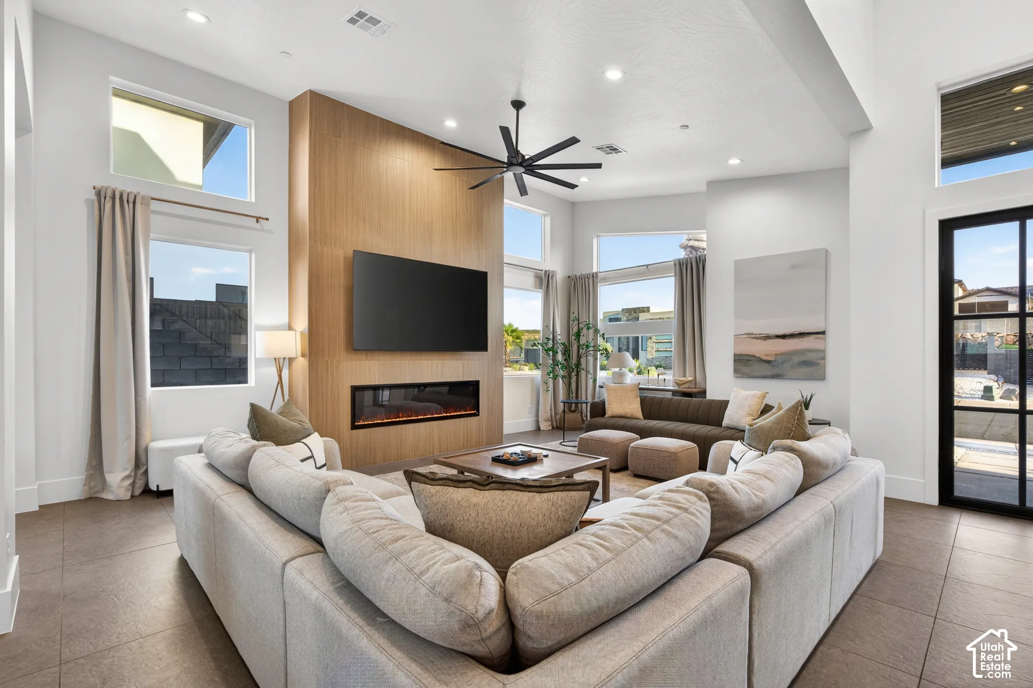 High ceilings with recessed lighting, large windows, wood-finish accent wall with an integrated electric fireplace, and dark-framed glass paneled door