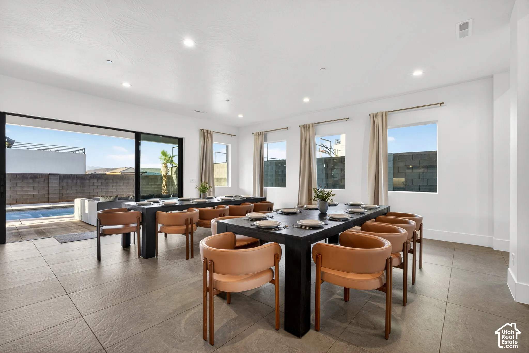 Expansive room with large format tile flooring, multiple windows with neutral drapery, recessed lighting, and a wide sliding glass door opening to an outdoor pool area