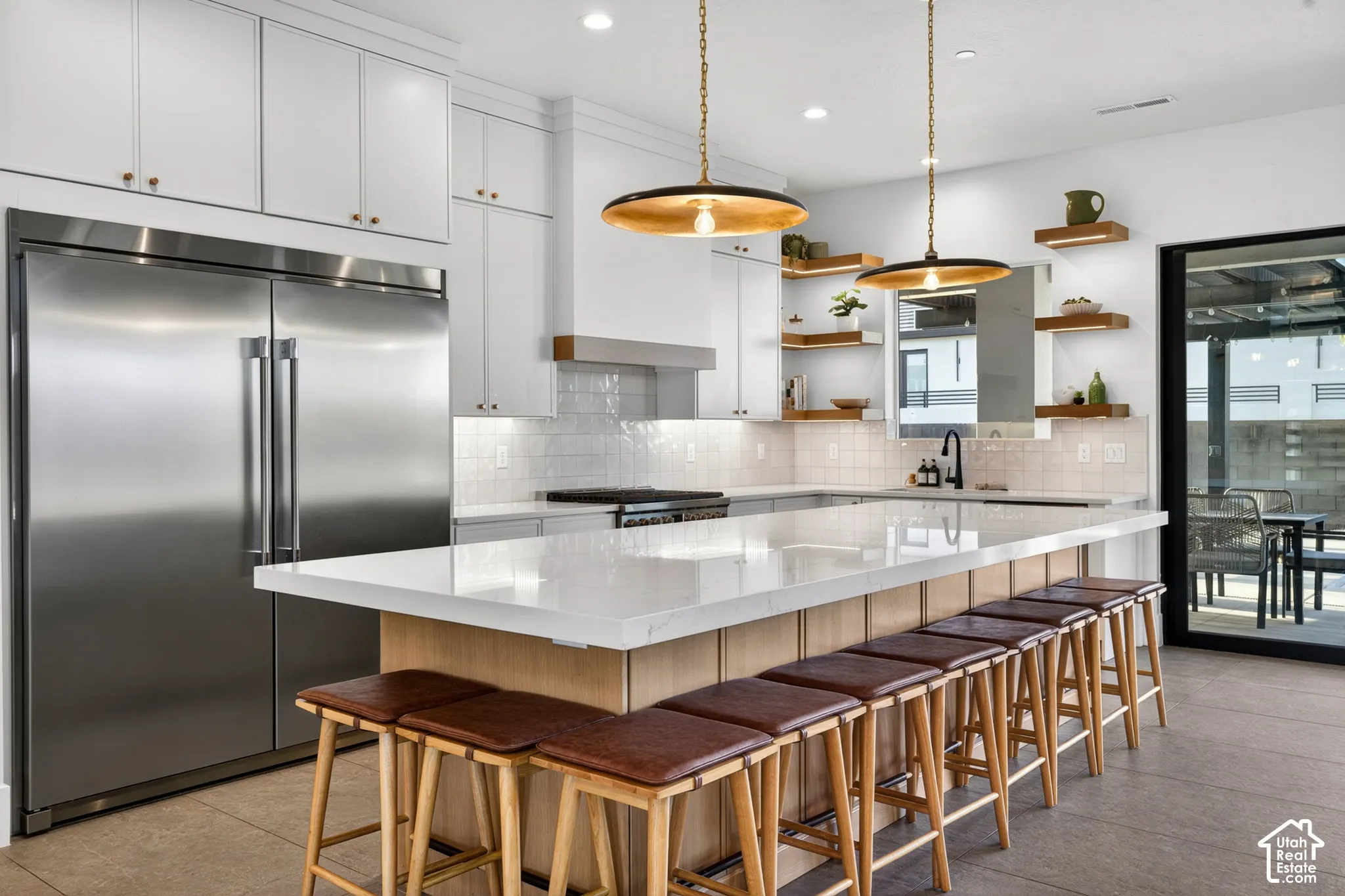 Expansive kitchen island with seating, stainless steel refrigerator, white shaker cabinetry, tiled backsplash, and recessed and pendant lighting