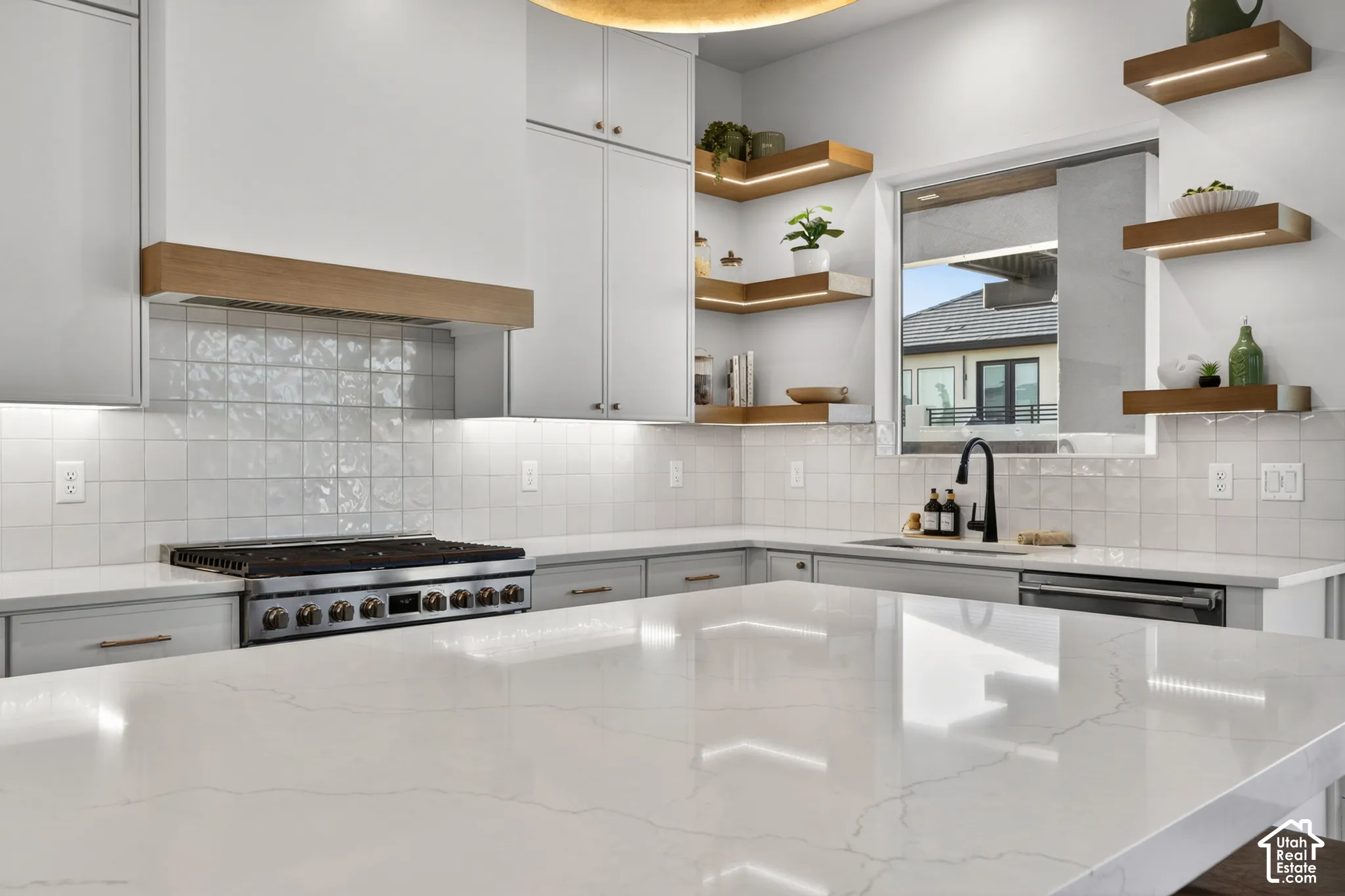 Kitchen featuring white cabinetry, light countertops, an integrated stainless steel range, a kitchen island, and open shelving with underlighting