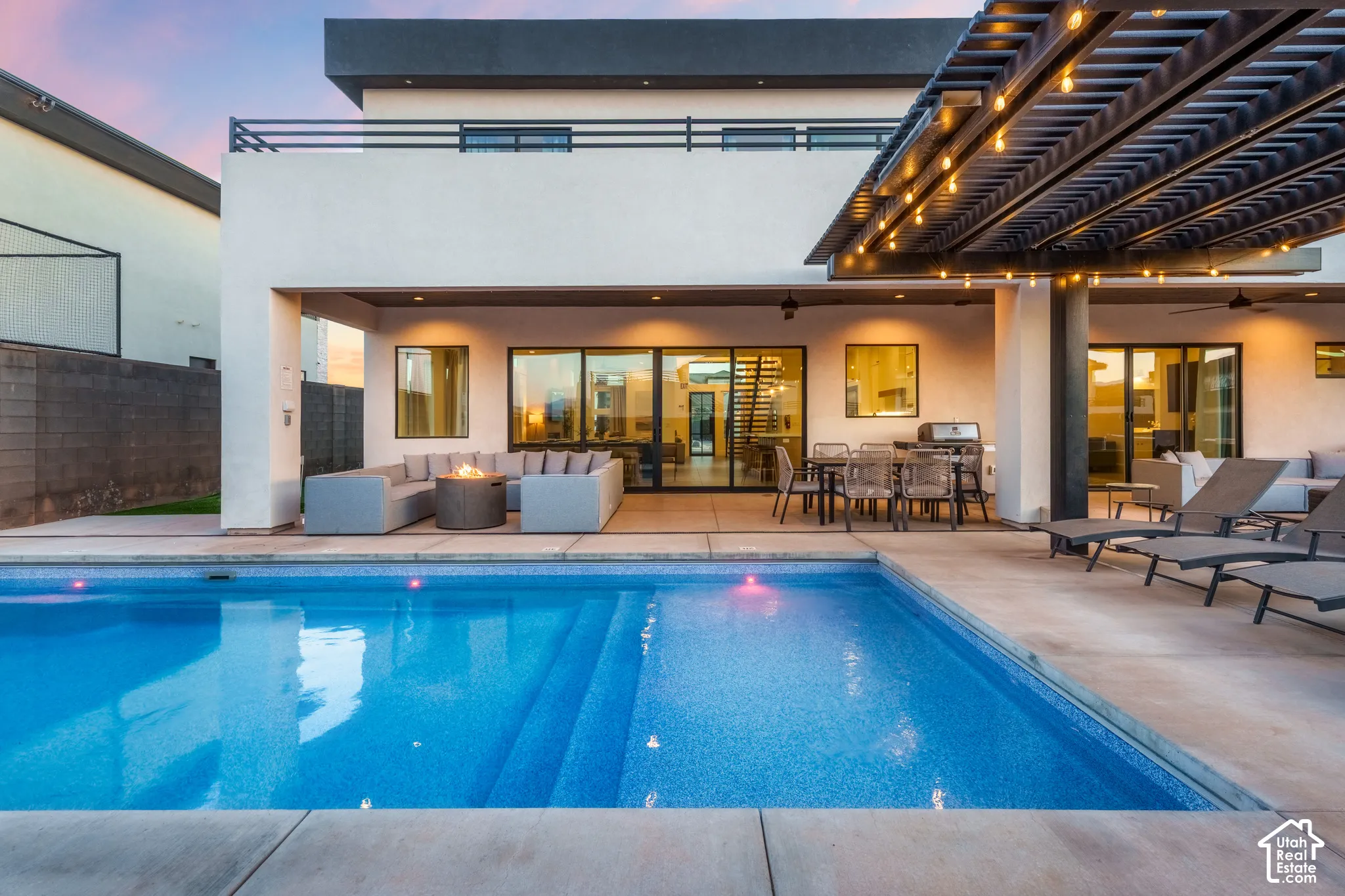Exterior with a swimming pool, large concrete patio, covered outdoor living area, second-story balcony with metal railing, and an integrated outdoor kitchen
