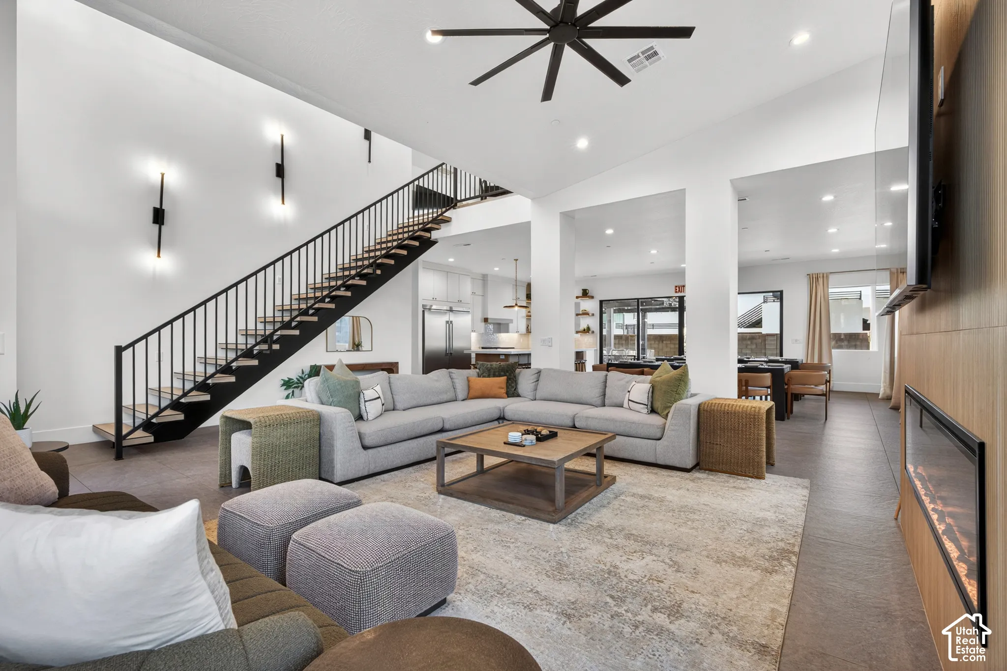 Vaulted ceilings with a ceiling fan, a floating staircase with metal railings, a linear fireplace with wood paneling, recessed lighting, and dark wood-finish flooring