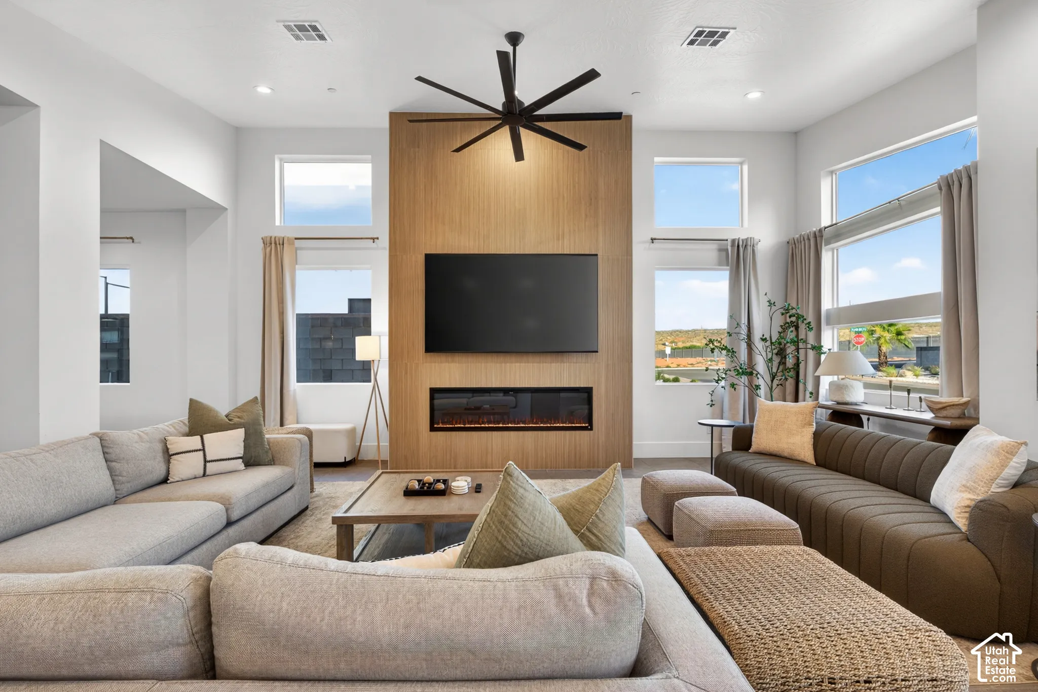 Vaulted ceilings in this living space with a wood-paneled accent wall, built-in linear fireplace, multiple windows with neutral drapery, and recessed lighting