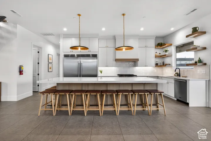 Kitchen featuring a large center island with seating, white cabinetry, stainless steel appliances, and integrated ceiling and pendant lighting