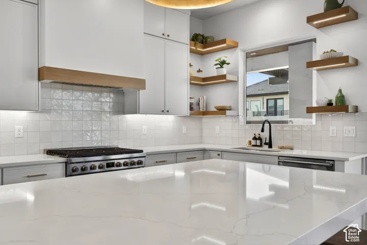 Kitchen featuring white cabinetry, light countertops, an integrated stainless steel range, a kitchen island, and open shelving with underlighting