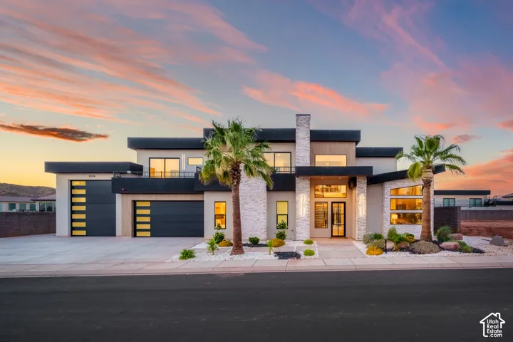 Modern architectural facade featuring stacked stone accents, multiple large windows, a prominent entry, a flat roofline, and integrated garage doors with horizontal glass panels