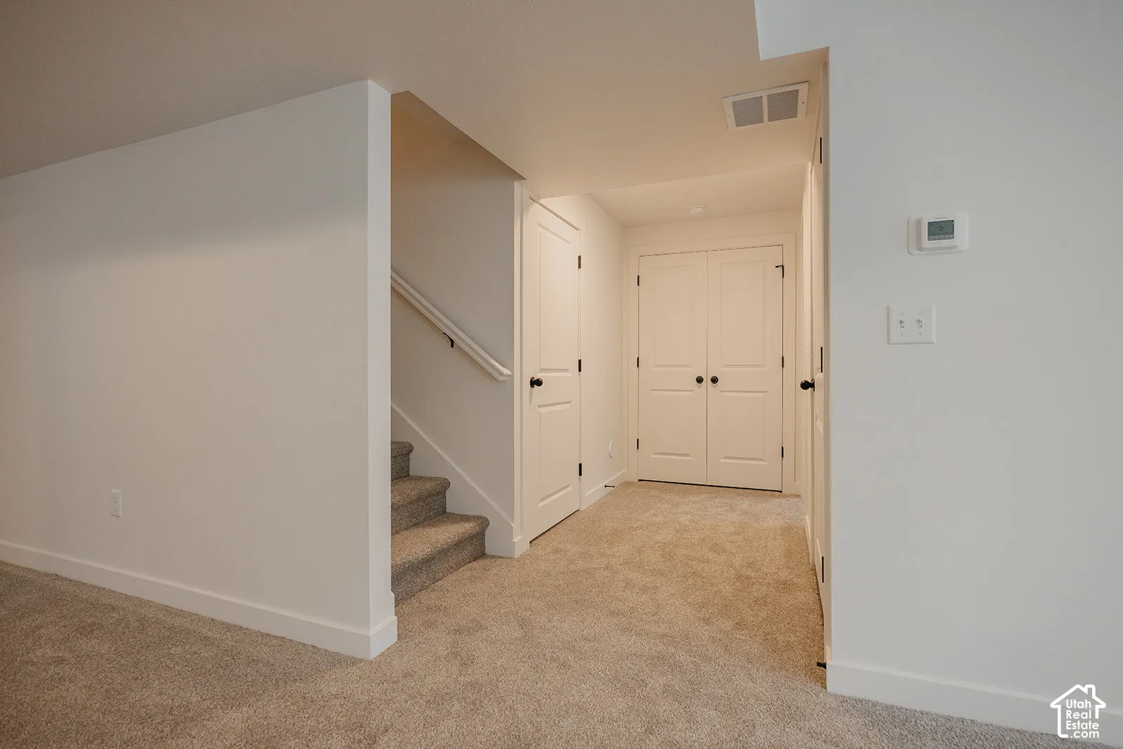 Carpeted stairway with a white handrail, leading to a carpeted hallway with painted bi-fold doors
