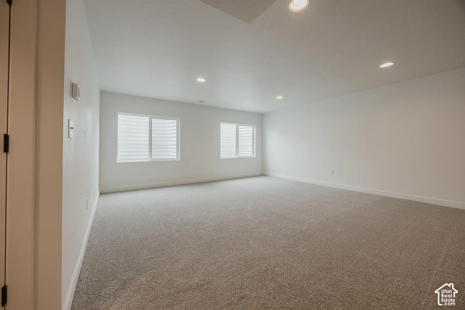 Recessed lighting, light-colored carpeting, white wall paint, multiple windows, and horizontal blinds