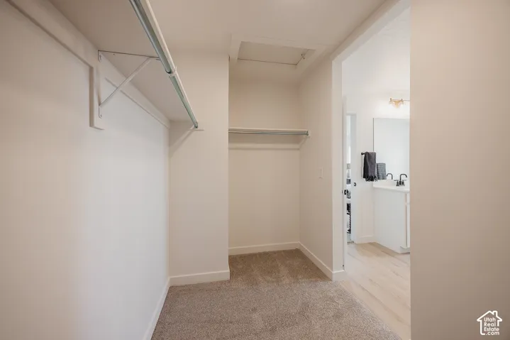Carpeted closet with dual hanging rods, built-in shelf, and access to a bathroom featuring a double vanity with matte black faucets