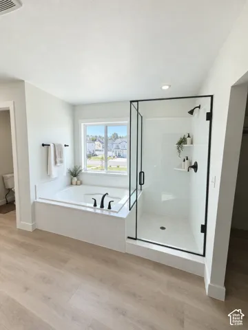 Built-in soaking tub with black fixtures, walk-in shower with clear glass enclosure and black frame, wood-finish flooring, and recessed ceiling lighting