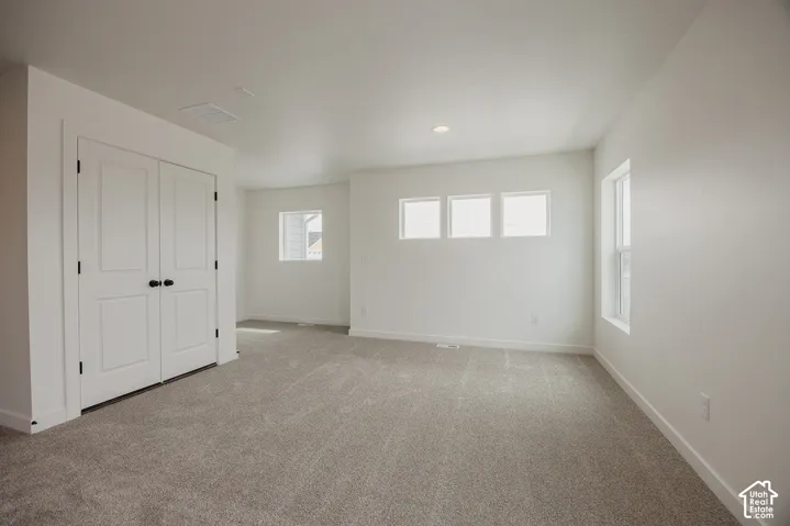 Neutral tone carpeting, multiple windows, double closet doors with dark hardware, recessed ceiling lighting