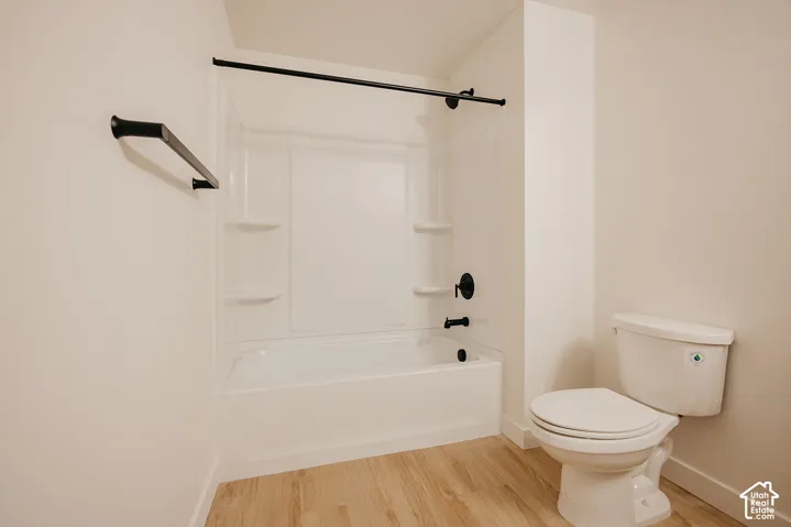 Bathtub with matte black fixtures and a sliding glass door frame, white toilet, and wood-finish flooring