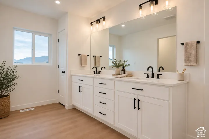 Dual vanity with white cabinetry, matte black hardware, and wood-finish flooring