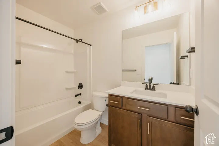 Bathroom featuring a shower-tub combination, vanity with an integrated sink, broad wall-mounted mirror, and wood-finish flooring