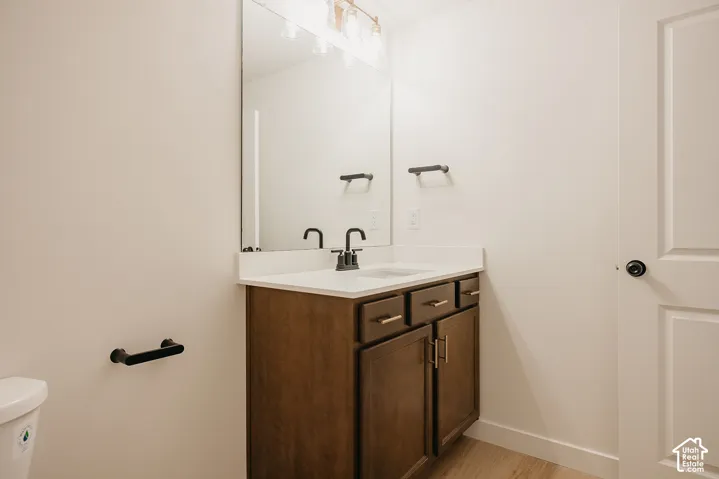 Wood-finish vanity with gold-tone hardware, white countertop with integrated sink, black-finish faucet, and a wall-mounted mirror