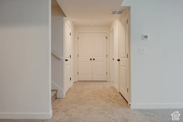 Carpeted hallway featuring white walls, white trim, and white doors with matte black hardware