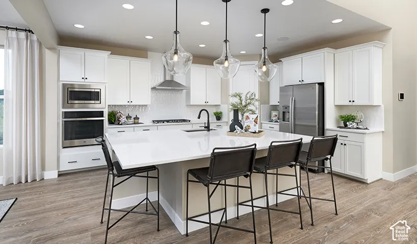 Open-concept kitchen featuring an oversized island with seating, stainless steel appliances, white shaker cabinetry, and wood-finish flooring