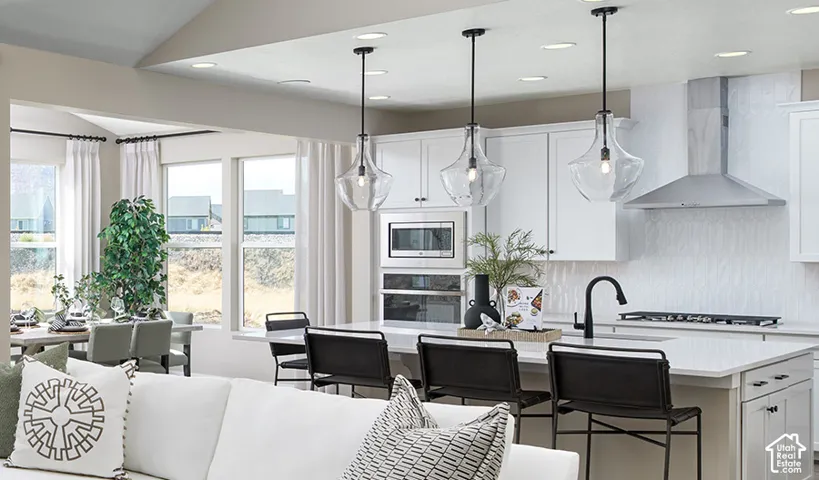 Kitchen island with seating for three, clear glass pendant lighting, stainless steel appliances, white cabinetry, and a dining area with multiple windows