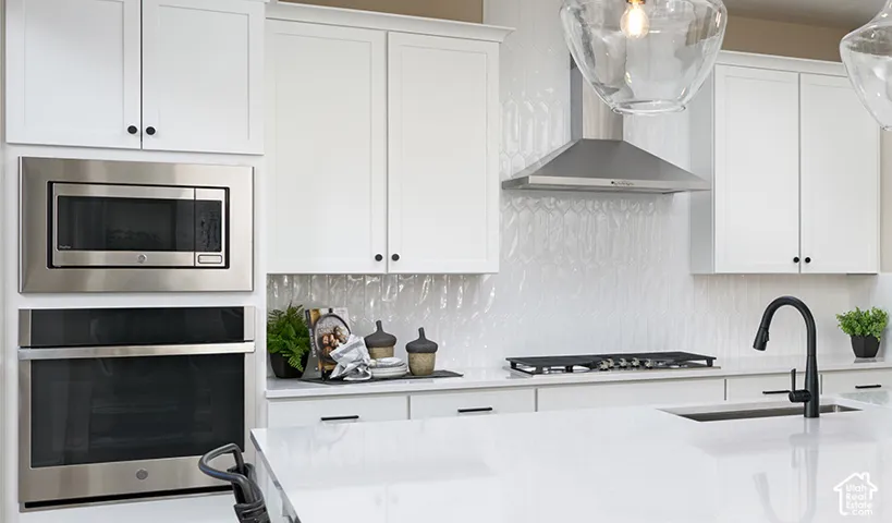 White shaker cabinetry, stainless steel appliances, integrated gas cooktop, textured tile backsplash, and a black gooseneck faucet