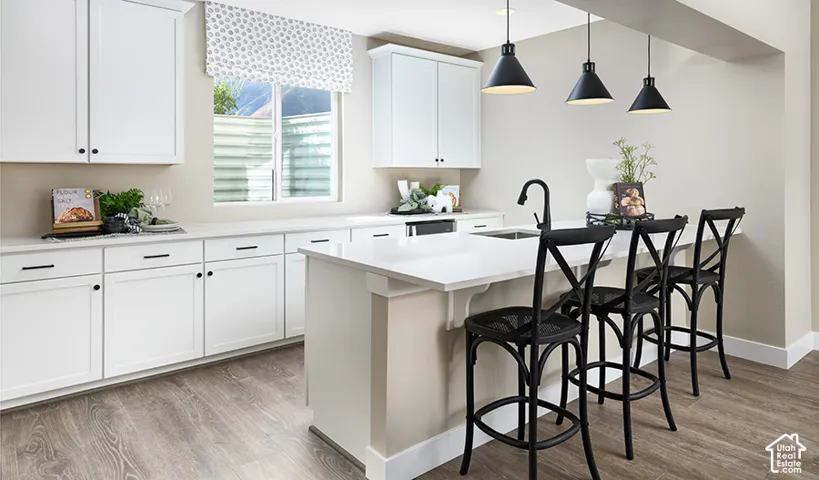Kitchen featuring white shaker-style cabinetry, a central island with a sink, pendant lighting, and wood-finish flooring