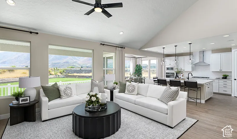 Vaulted ceiling with a ceiling fan, expansive windows, light wood-finish flooring, white cabinetry, and stainless steel kitchen appliances