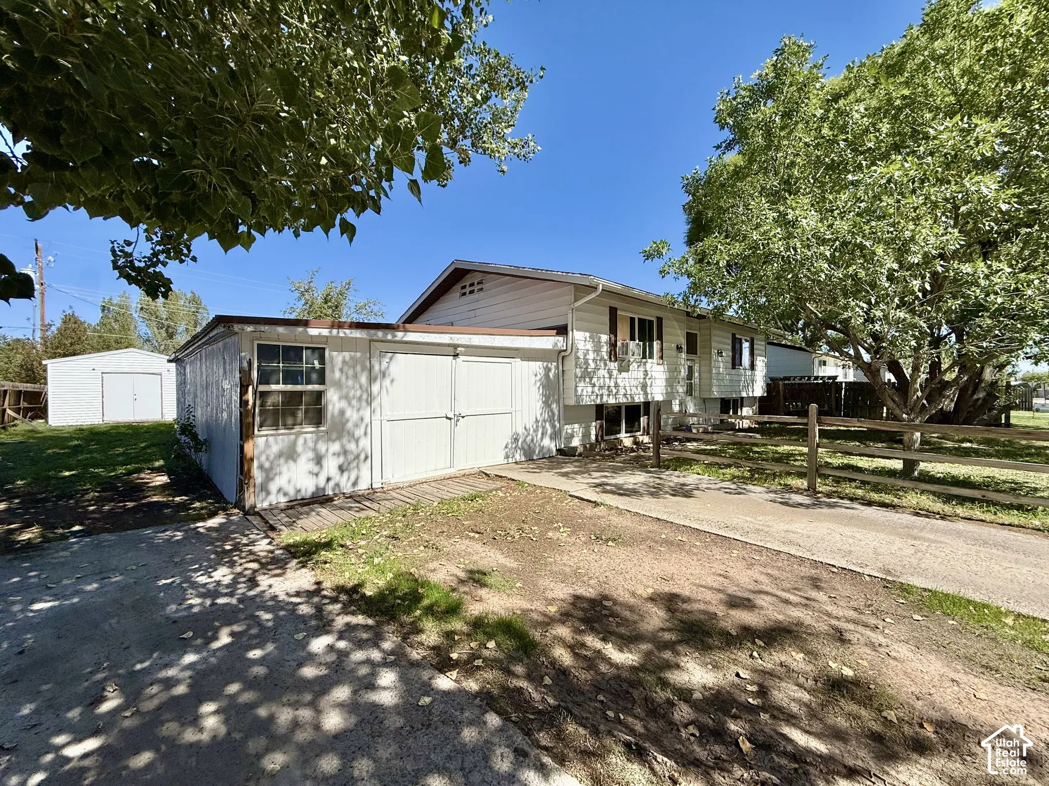 Property exterior featuring white siding, a split-rail fence, a concrete driveway, a detached shed with double doors, and an additional white detached garage
