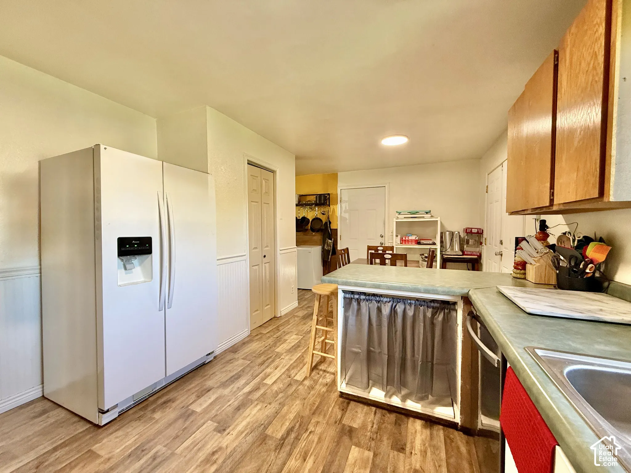 Wood-finish flooring, white beadboard wainscoting, light wood-tone cabinetry, and a countertop with an integrated sink