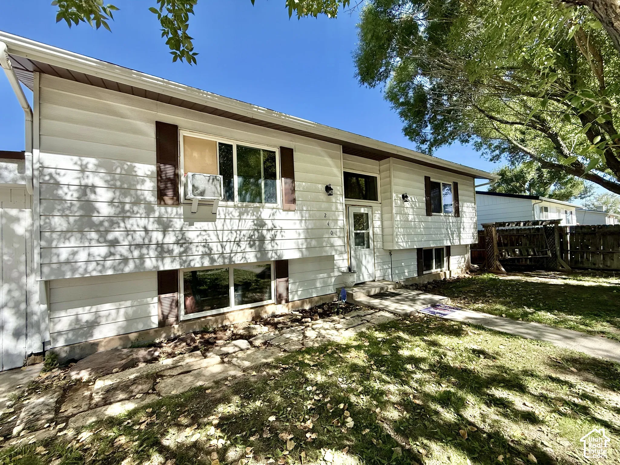 White horizontal siding exterior with brown trim accents, featuring multiple windows and a front entry door with a storm door