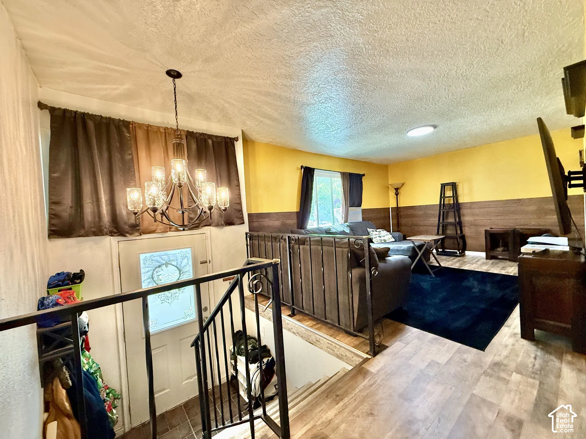 Wood-finish flooring, half-wall wood paneling, decorative metal railing, a ten-light chandelier, and a front entry door with privacy glass