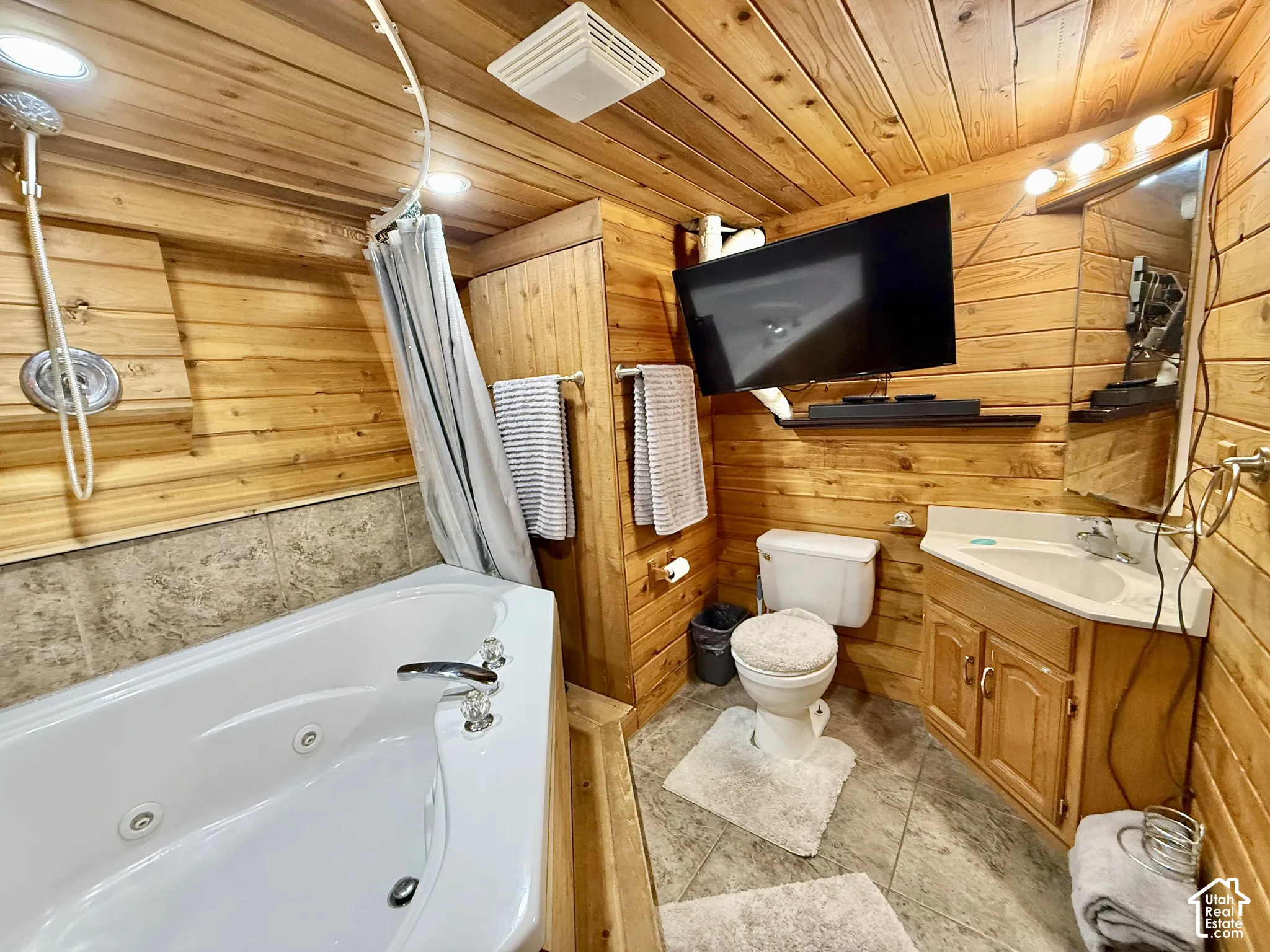 Wood-paneled bathroom featuring a jetted tub, ceramic tile flooring, built-in vanity with single basin sink, and recessed lighting