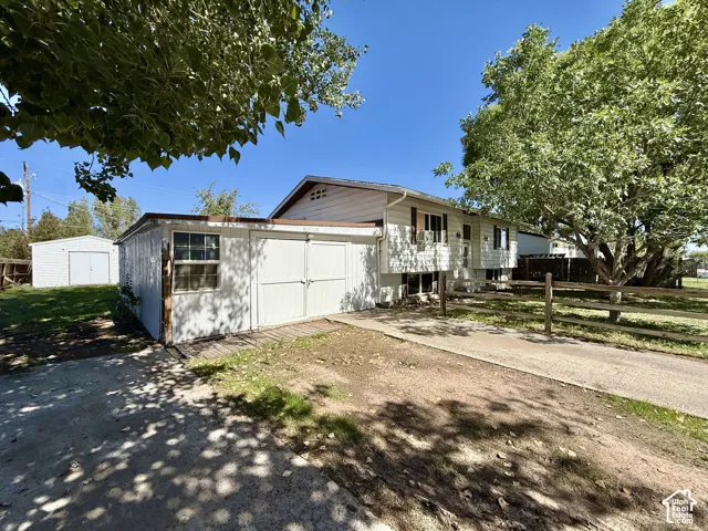 Property exterior featuring white siding, a split-rail fence, a concrete driveway, a detached shed with double doors, and an additional white detached garage