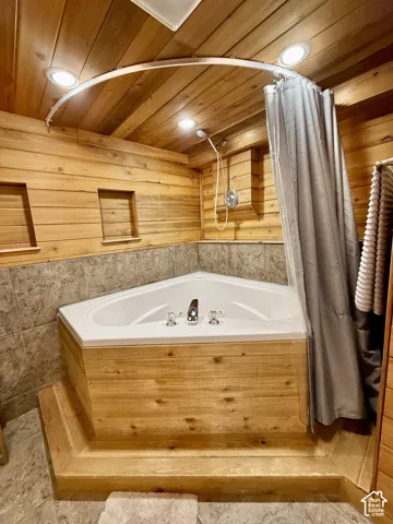 Corner soaking tub with integrated shower, wood-paneled walls and ceiling, recessed lighting, and tiled flooring