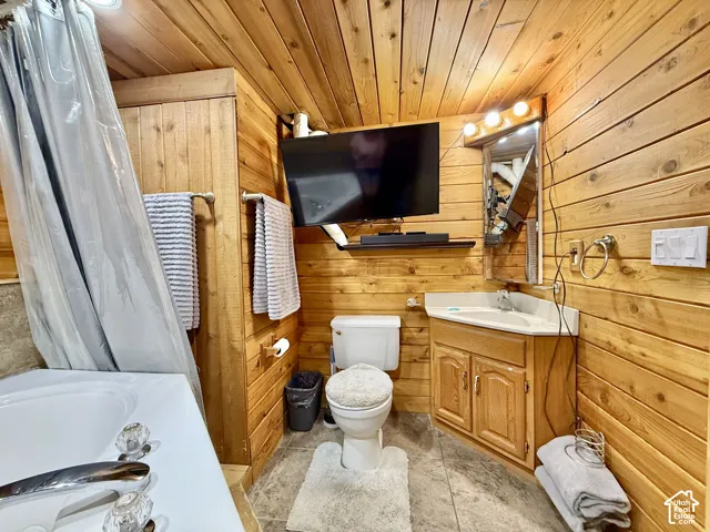 Wood-paneled walls and ceiling, white tub with chrome fixtures, corner vanity with wood-finish cabinetry, and a surface-mount mirror with bar lighting