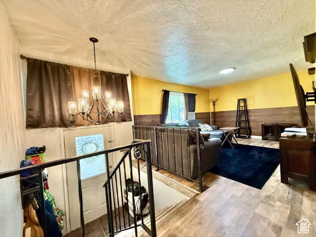Wood-finish flooring, half-wall wood paneling, decorative metal railing, a ten-light chandelier, and a front entry door with privacy glass
