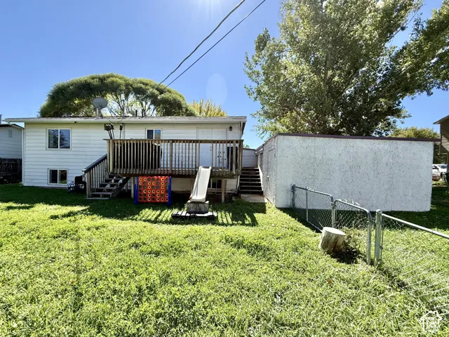 Rear exterior featuring a wood deck with stairs, white siding, and an adjacent stucco-sided shed