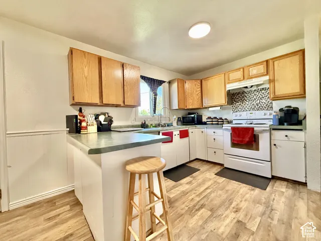 Kitchen featuring wood-finish flooring, light wood cabinetry, a tiled backsplash, and a built-in range with a microwave hood